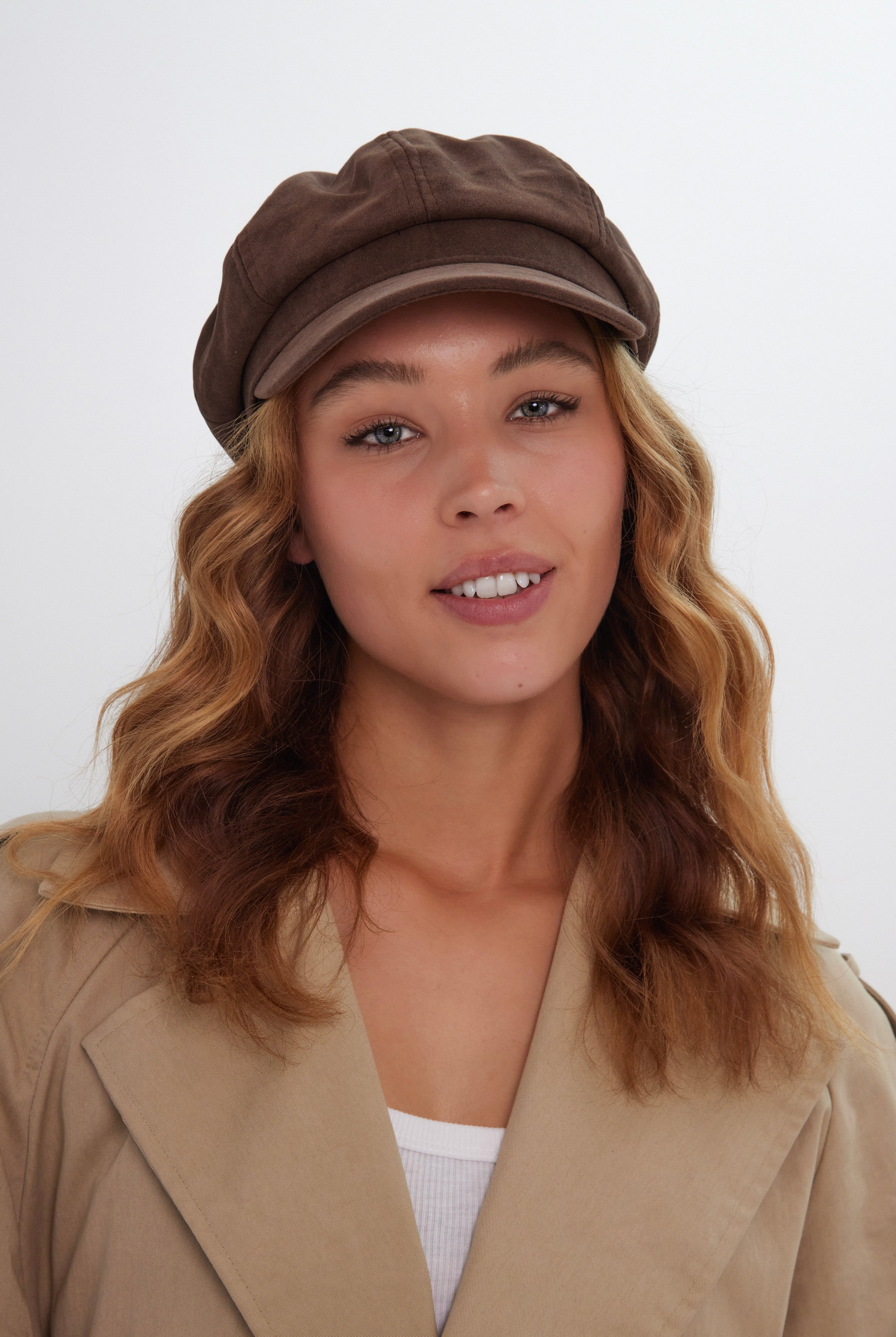 Woman wearing a brown suede baker boy cap and beige coat on a white background
