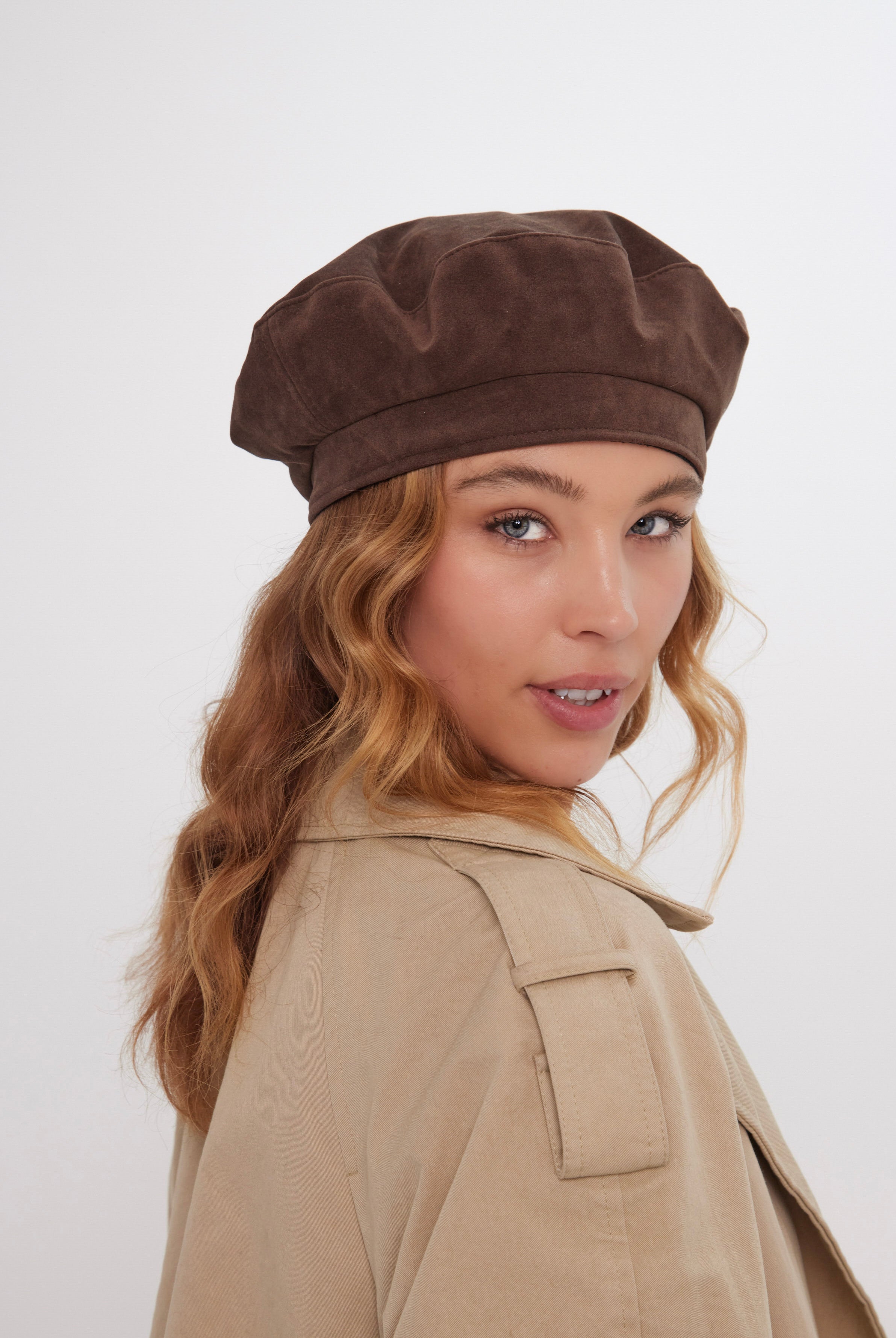 Woman wearing a brown suede beret and beige coat on a white background