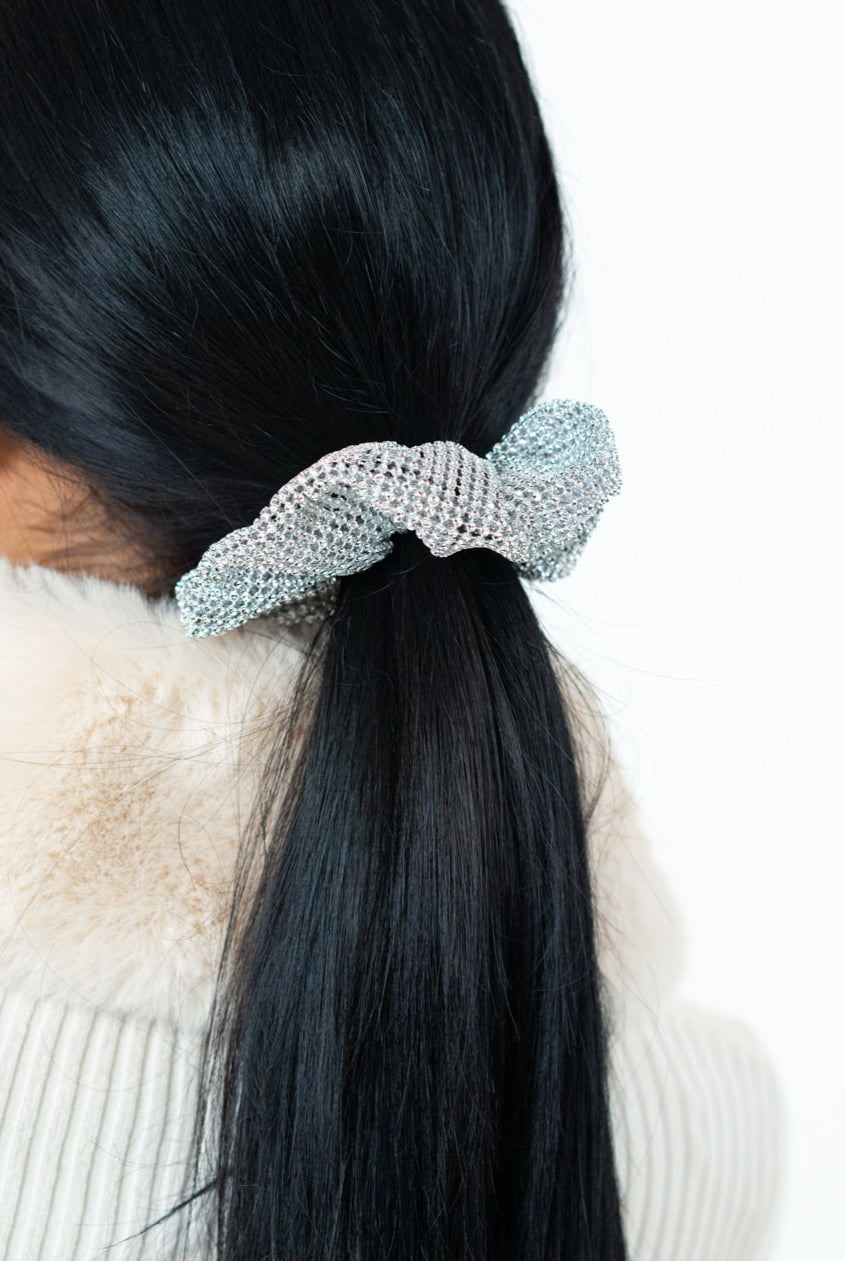 Person with long black hair tied in a ponytail using a decorative hair tie against a white background