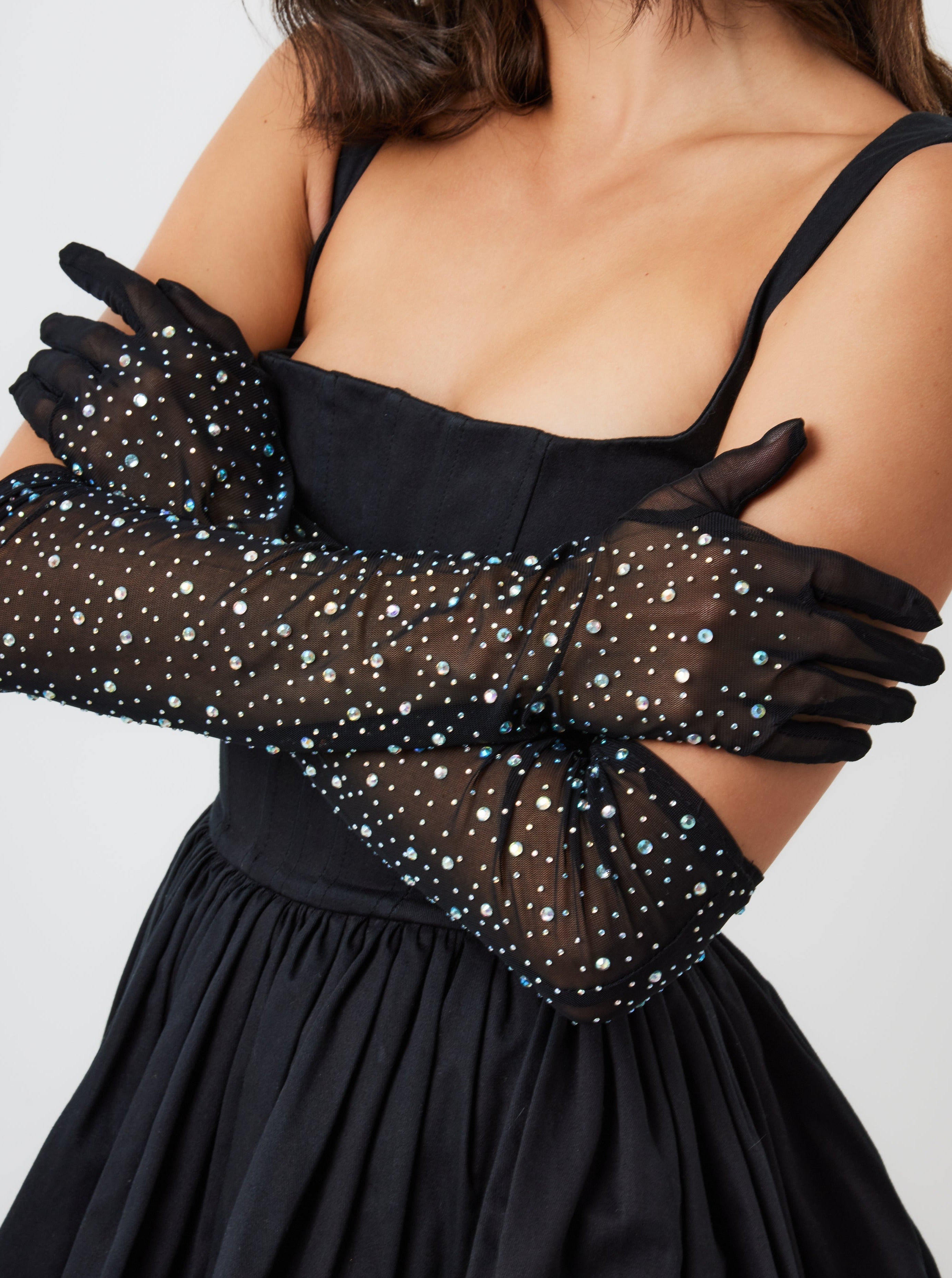 A woman wearing black over-the-elbow mesh gloves embellished with rhinestones.