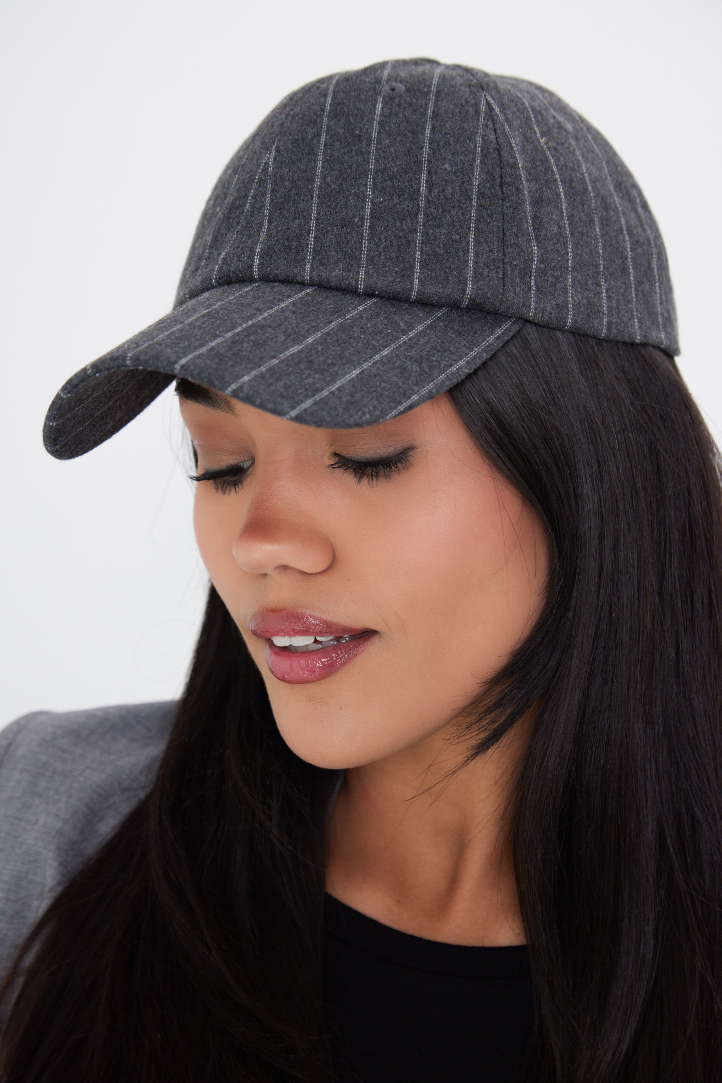 A woman wearing a charcoal grey pinstripe baseball cap with an adjustable metal back fastening.