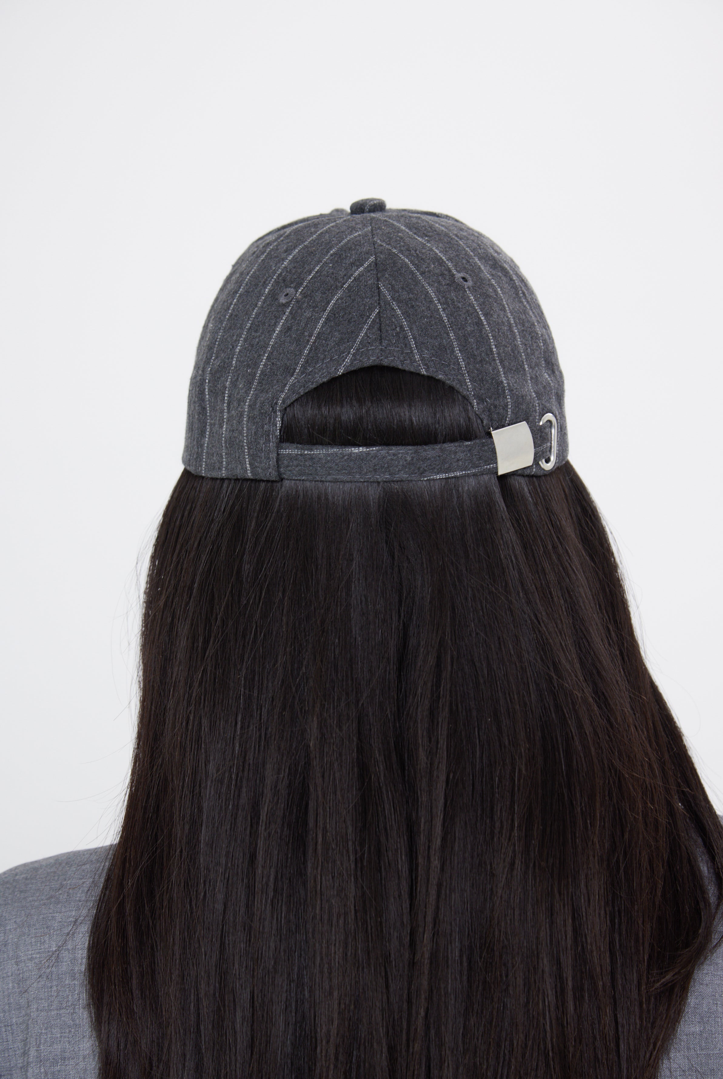 A woman wearing a charcoal grey pinstripe baseball cap with an adjustable metal back fastening.