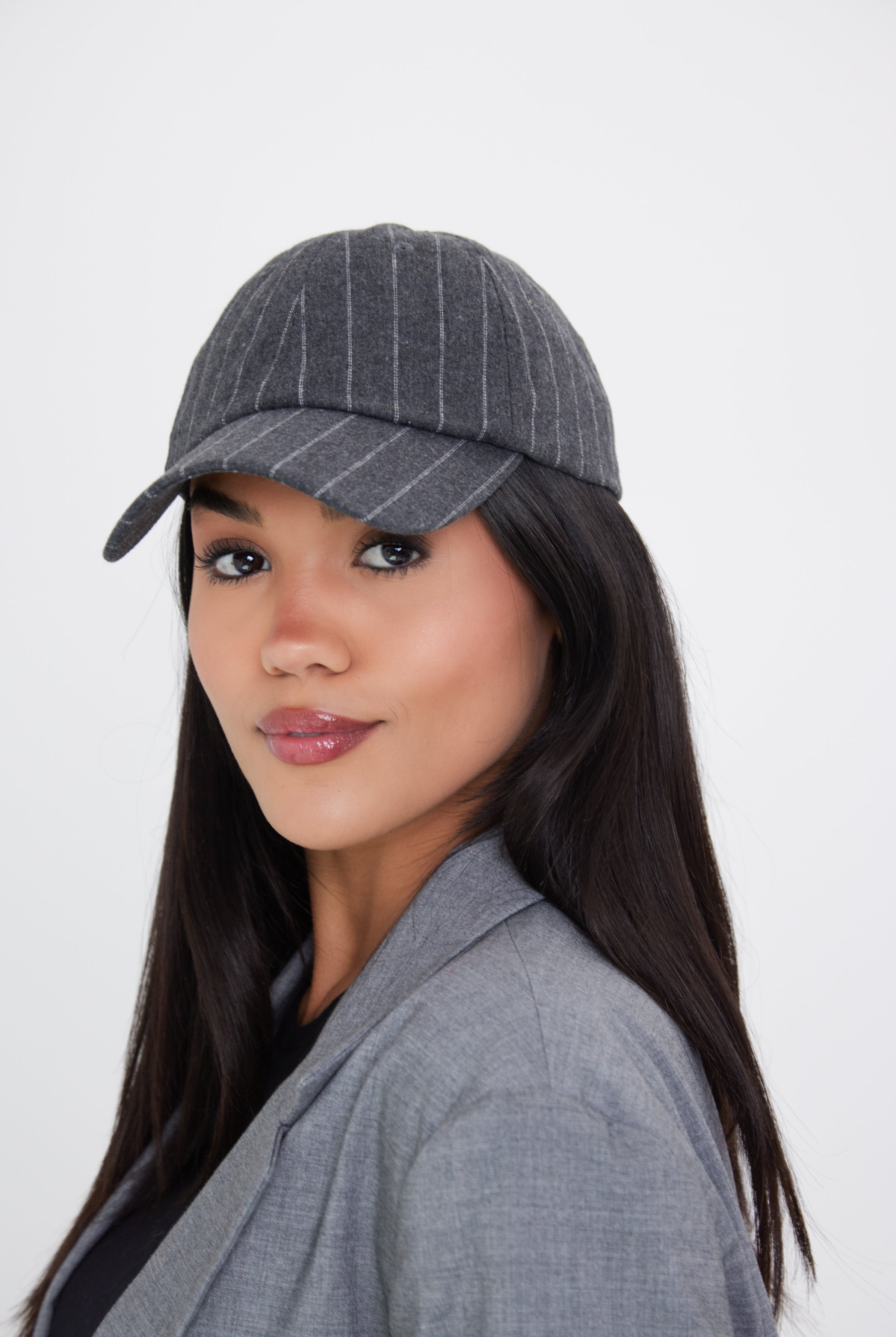 A woman wearing a charcoal grey pinstripe baseball cap with an adjustable metal back fastening.