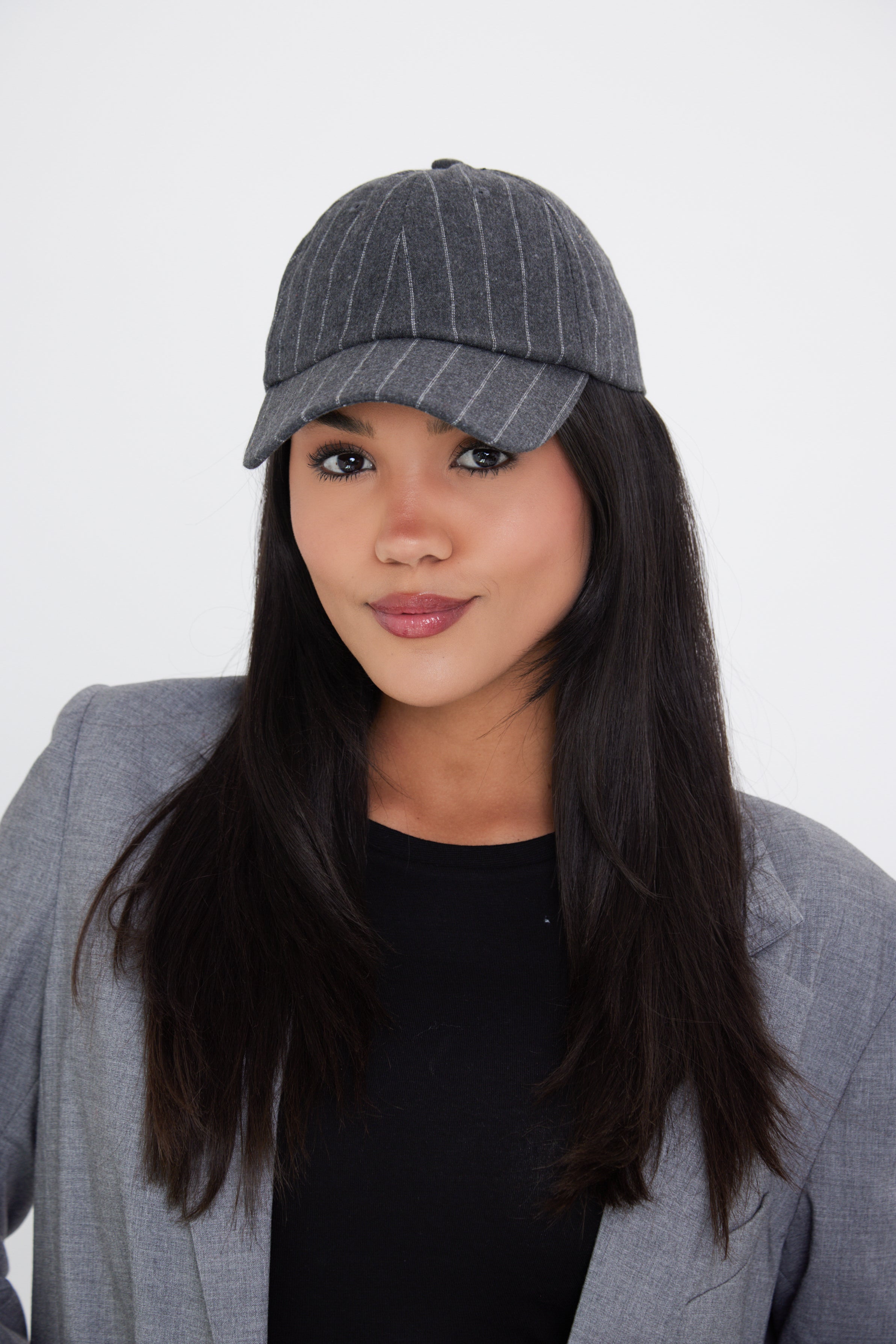 A woman wearing a charcoal grey pinstripe baseball cap with an adjustable metal back fastening.