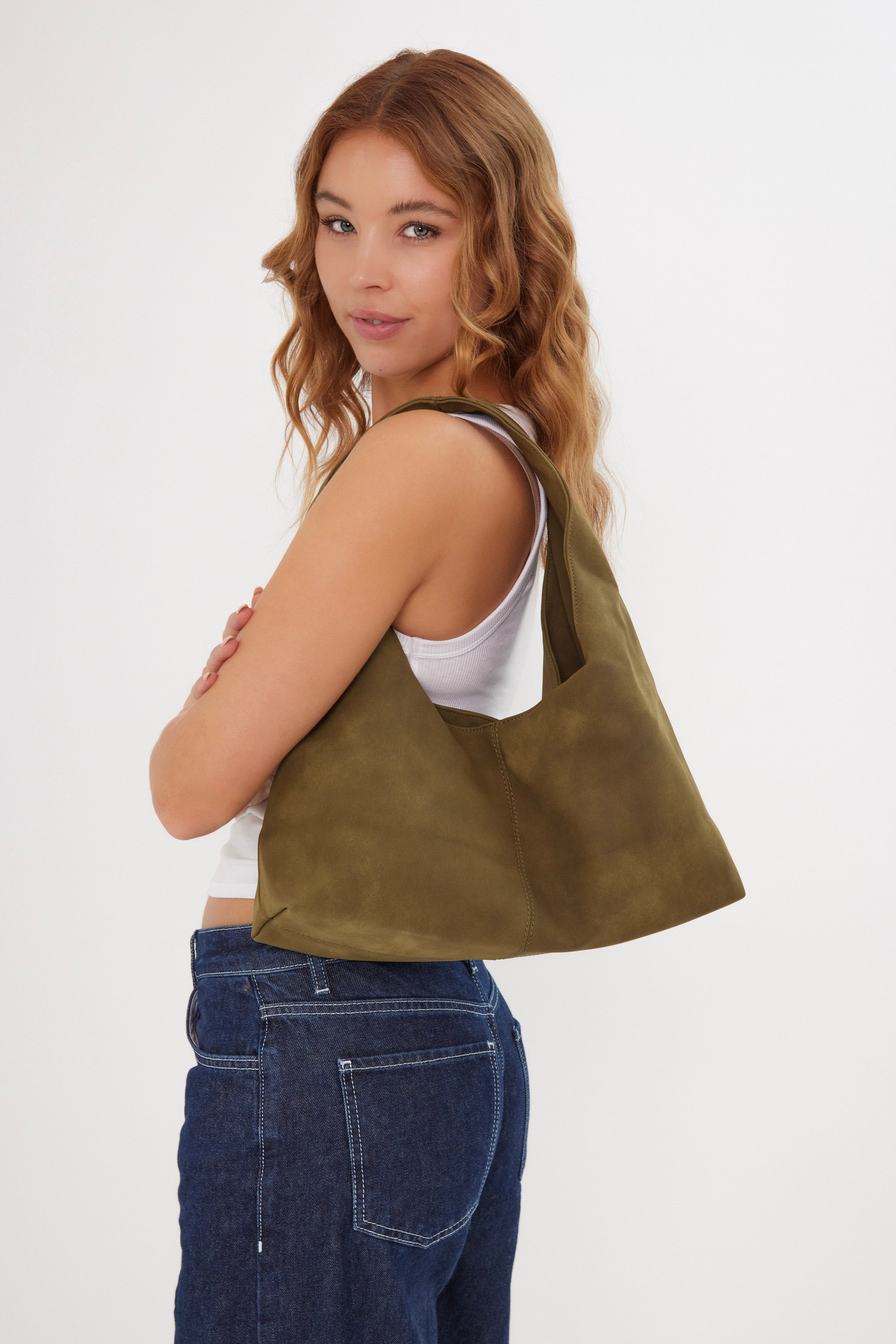 Woman carrying a green suede shoulder bag on a white background