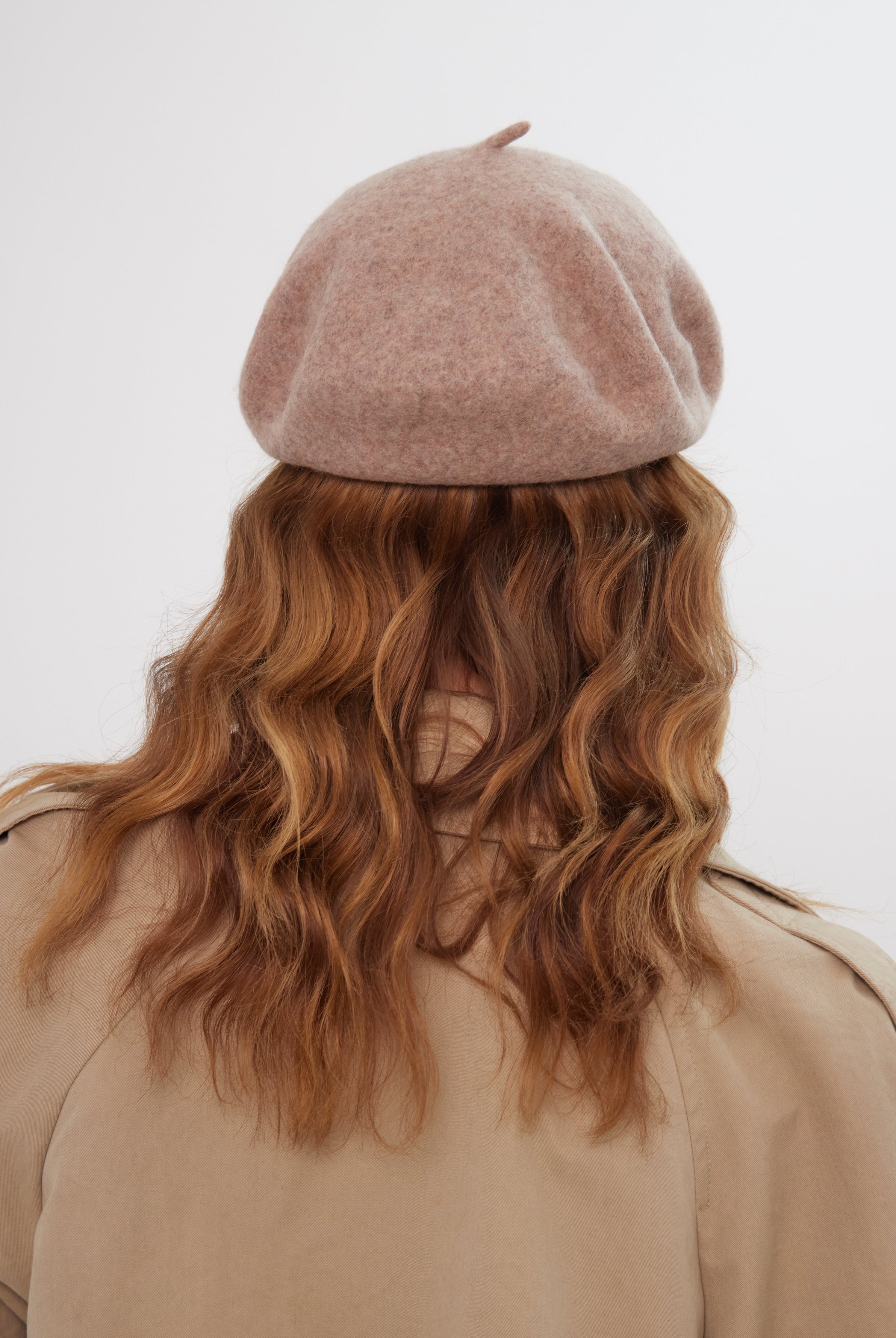 Person wearing a beige beret and coat with wavy hair on a light background
