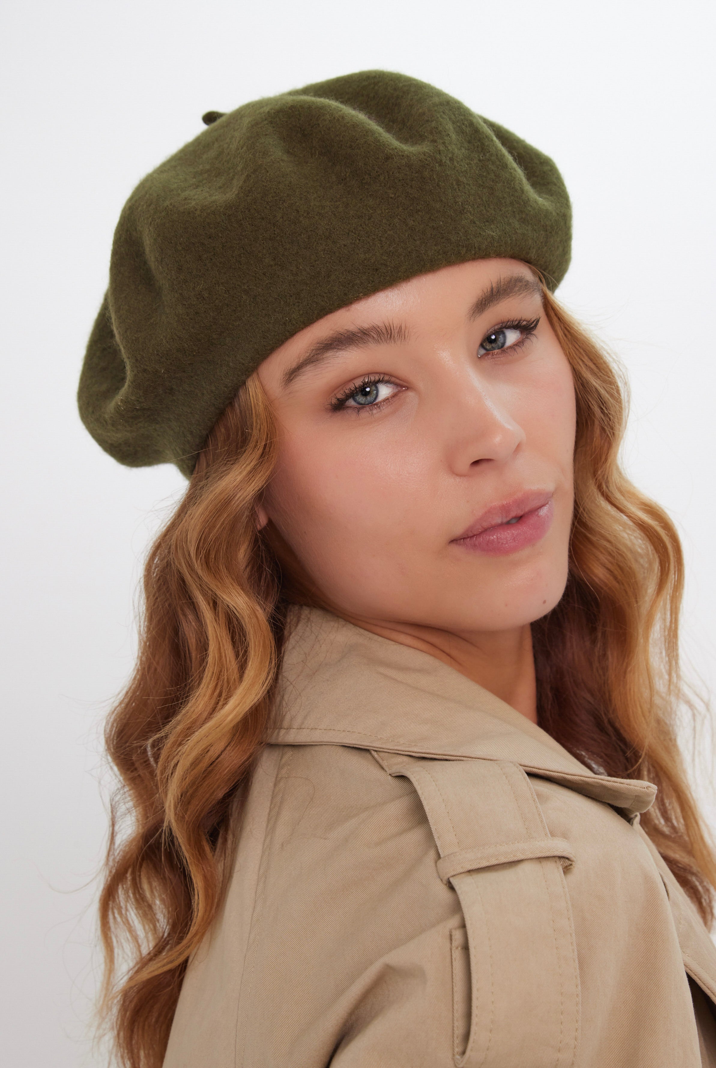 Woman wearing an olive green beret and beige coat on a white background