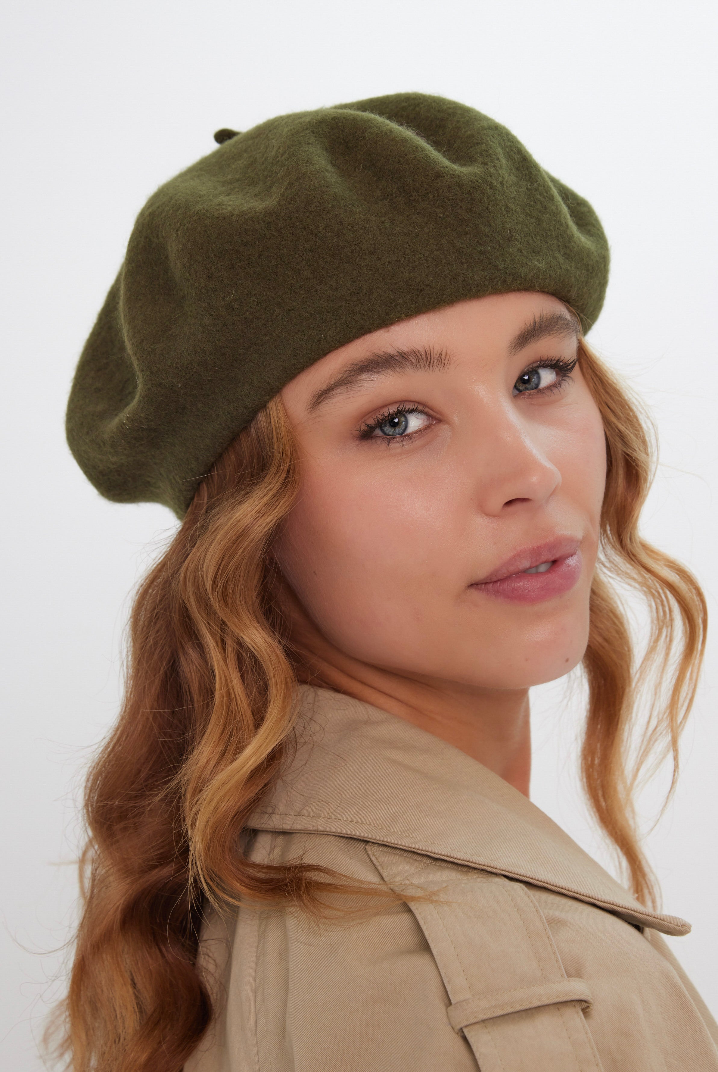 Woman wearing a green beret and beige coat against a white background