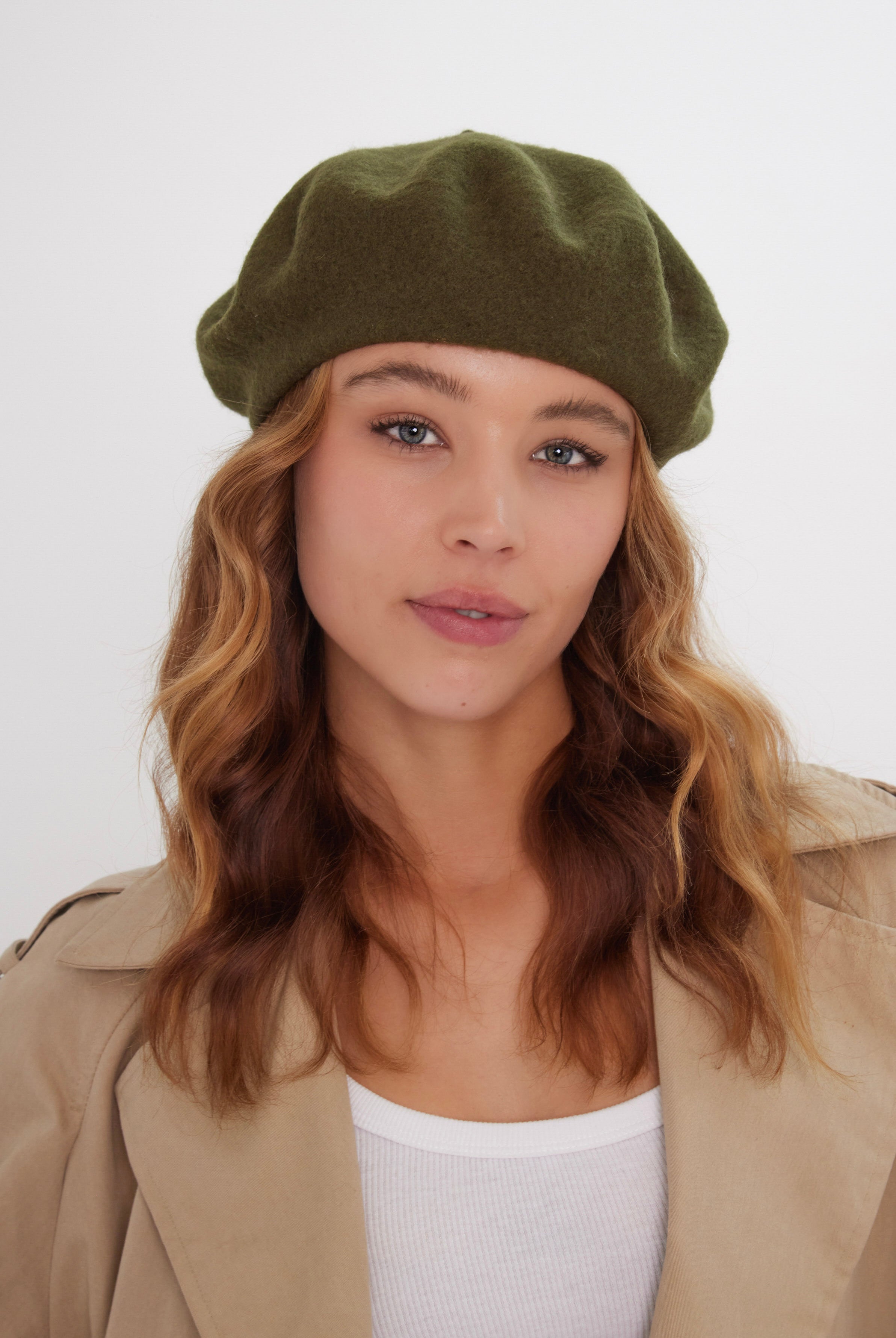 Woman wearing a green beret and beige coat against a white background