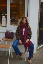 Woman sitting on a chair wearing a red scarf and blue jeans, with a purple handbag nearby.