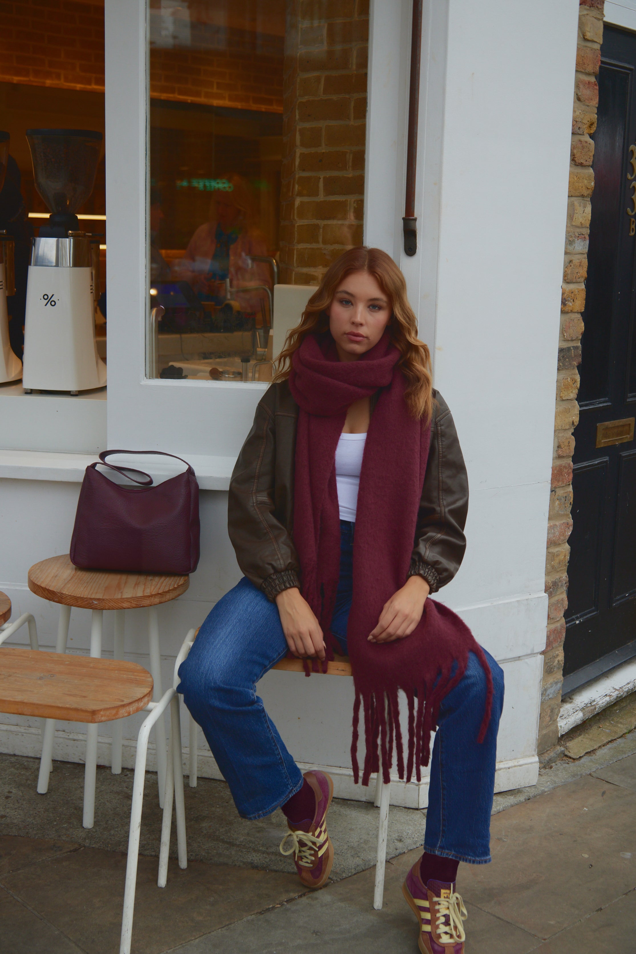 Woman sitting on a chair wearing a red scarf and blue jeans, with a purple handbag nearby.
