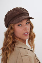 Woman wearing a brown suede baker boy cap and beige jacket on a white background