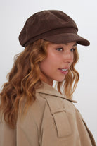 Woman wearing a brown suede baker boy cap and beige coat on a white background
