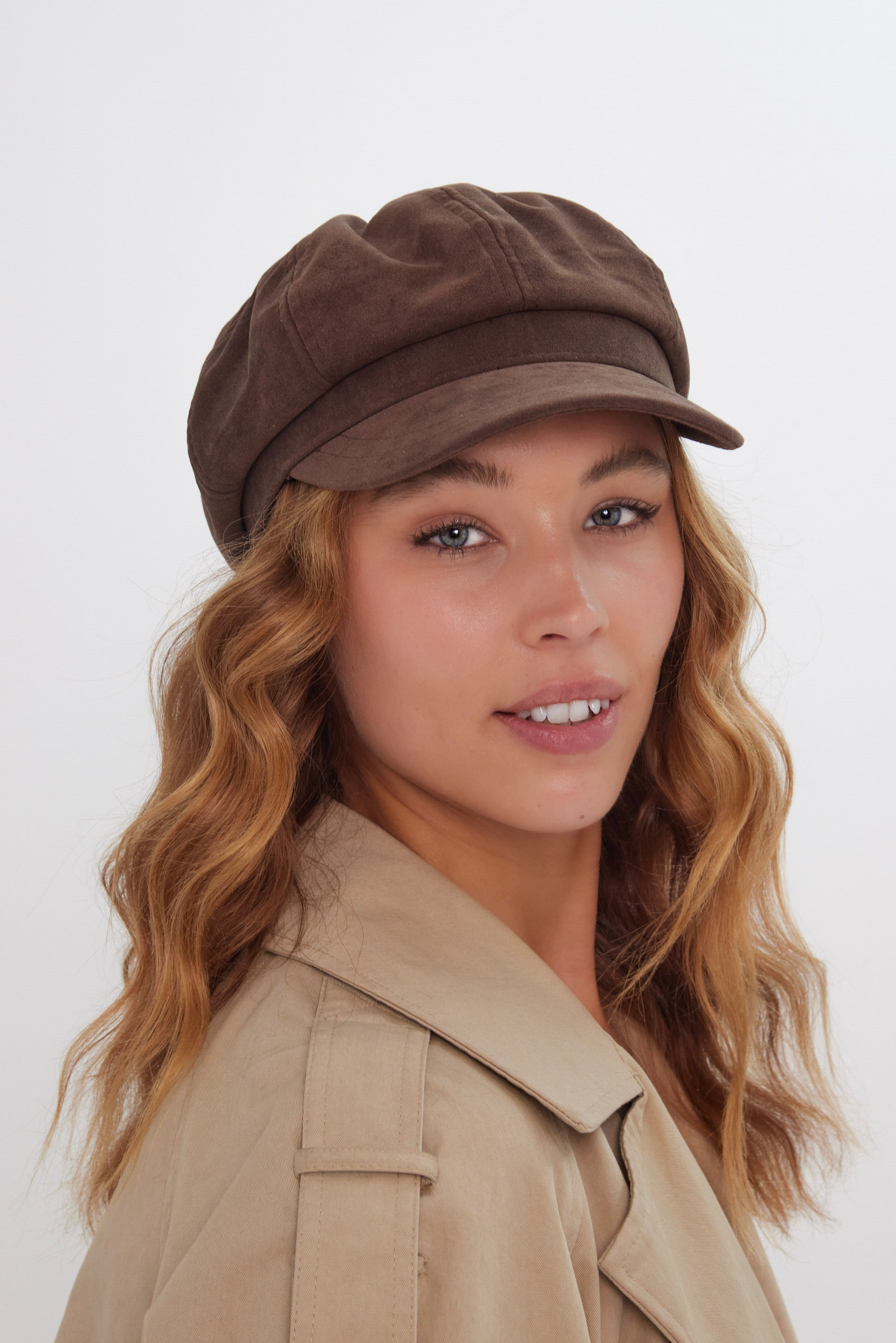 Woman wearing a brown suede baker boy cap and beige coat on a white background