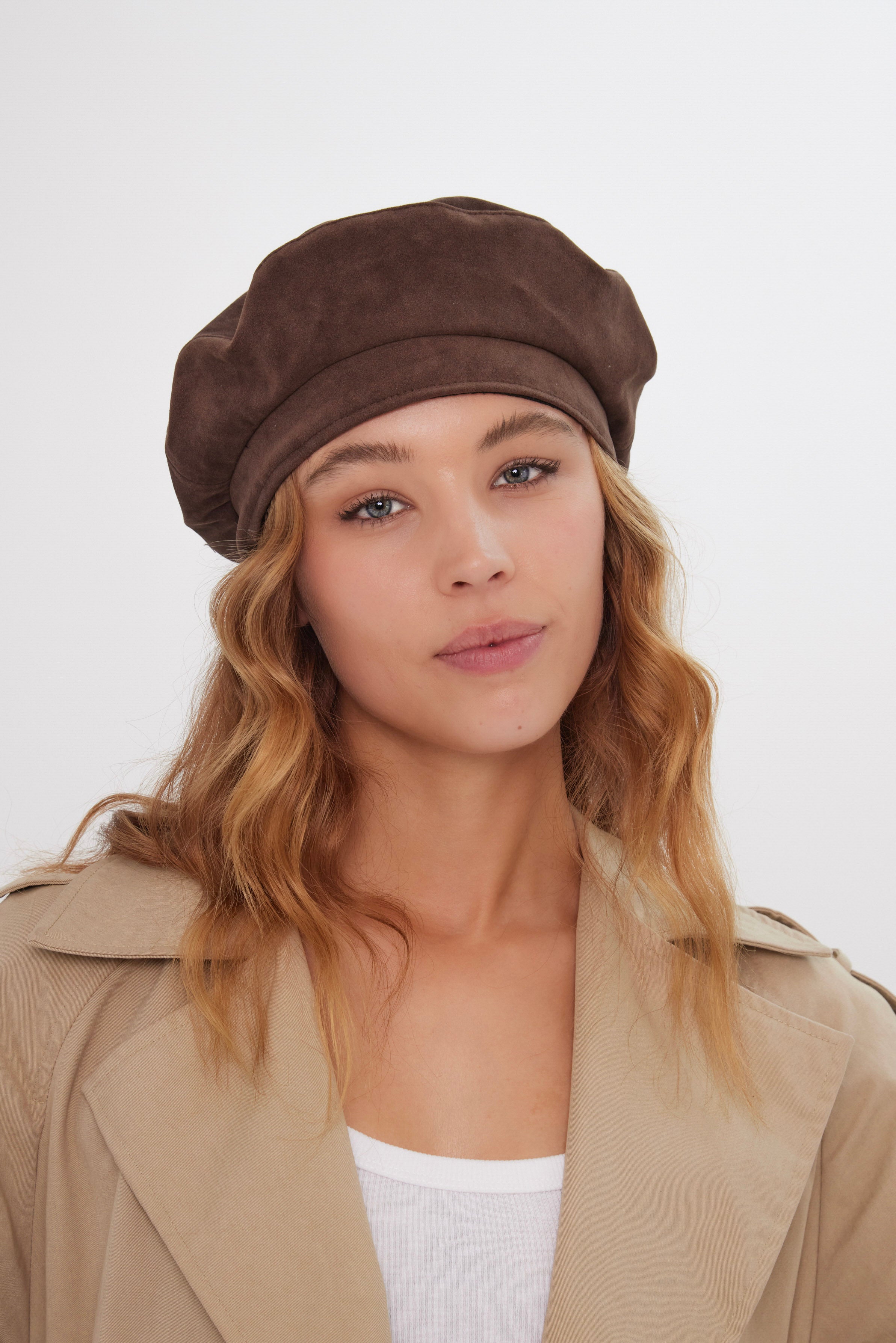 Woman wearing a brown beret and beige trench coat against a white background