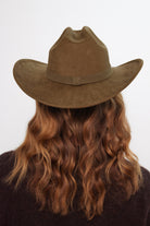 Person wearing a green suede hat with long wavy hair on a white background