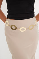 Person wearing a gold belt with circular designs on a plain background