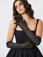 A woman wearing black over-the-elbow mesh gloves embellished with rhinestones.