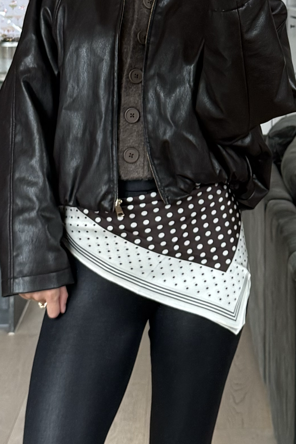 Person wearing a black leather jacket with a polka dot scarf, standing outdoors.