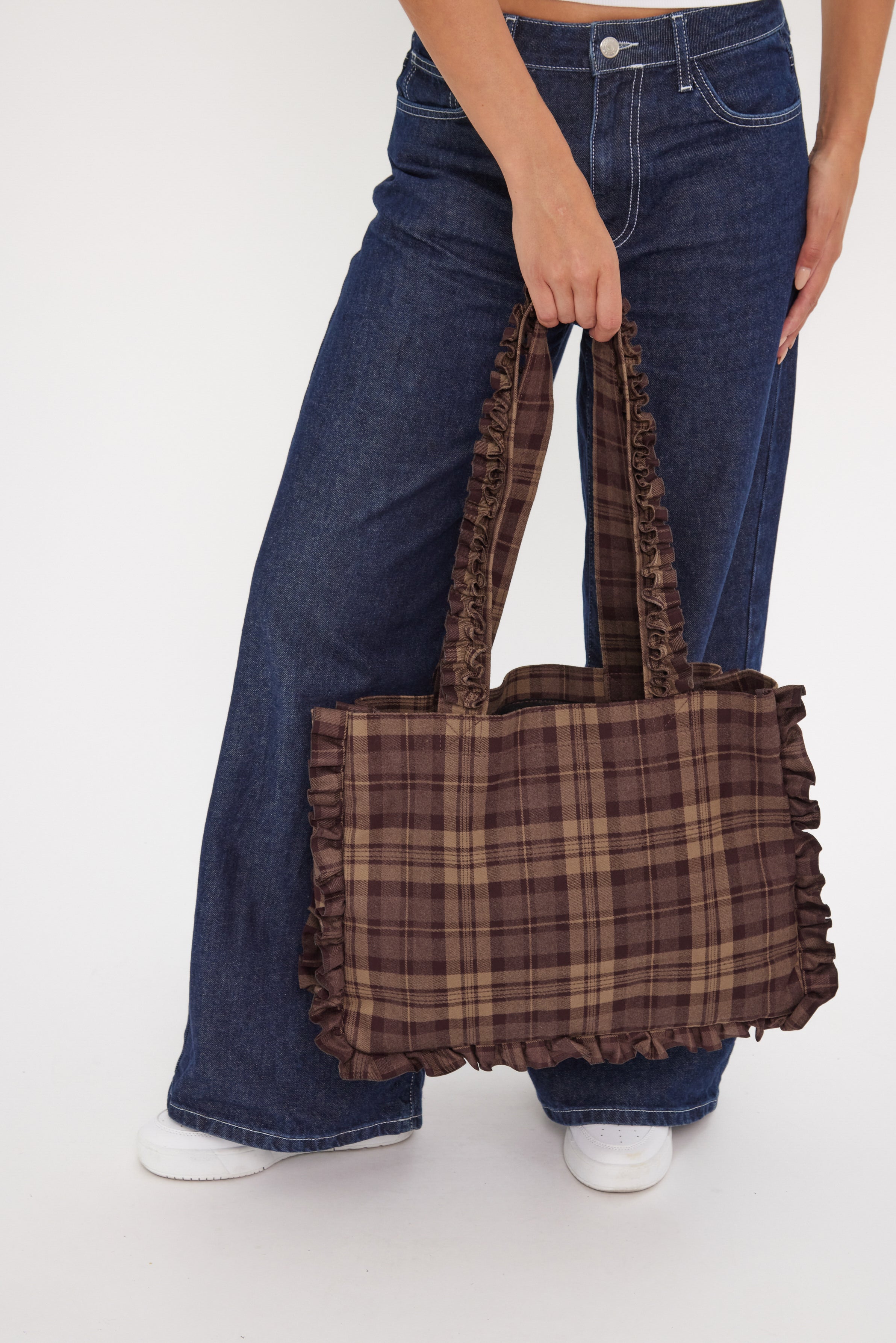 Person holding a brown plaid bag with blue jeans on a white background