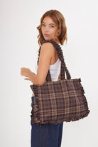 Woman holding a plaid check burgundy bag on a white background