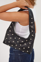 Woman holding a black studded handbag against a white background