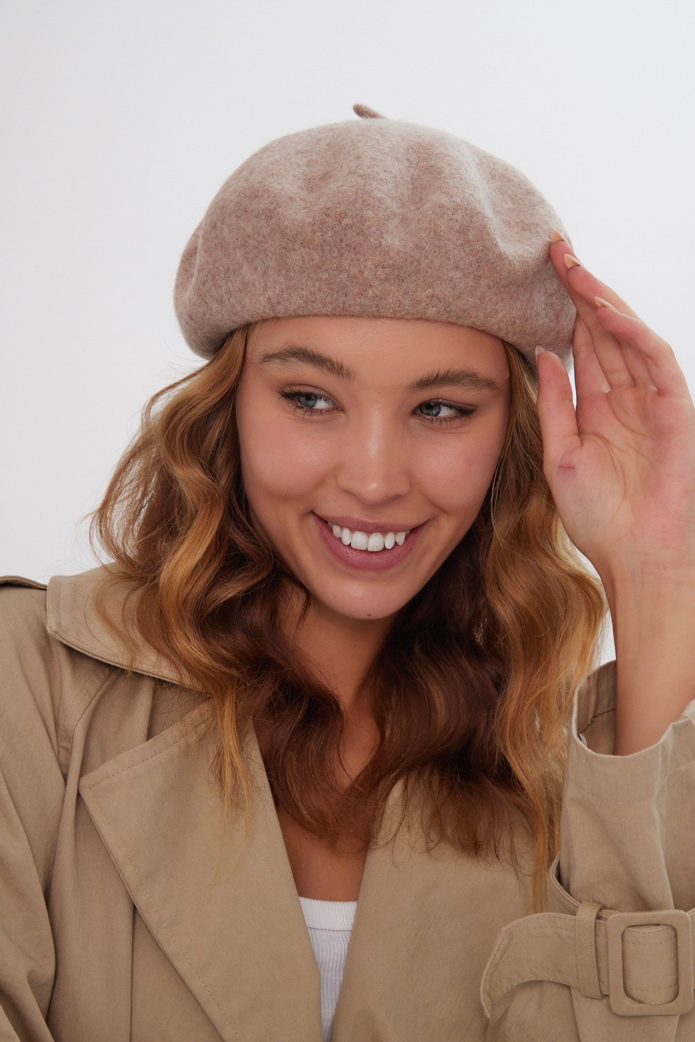 Woman wearing a beige beret and coat against a white background