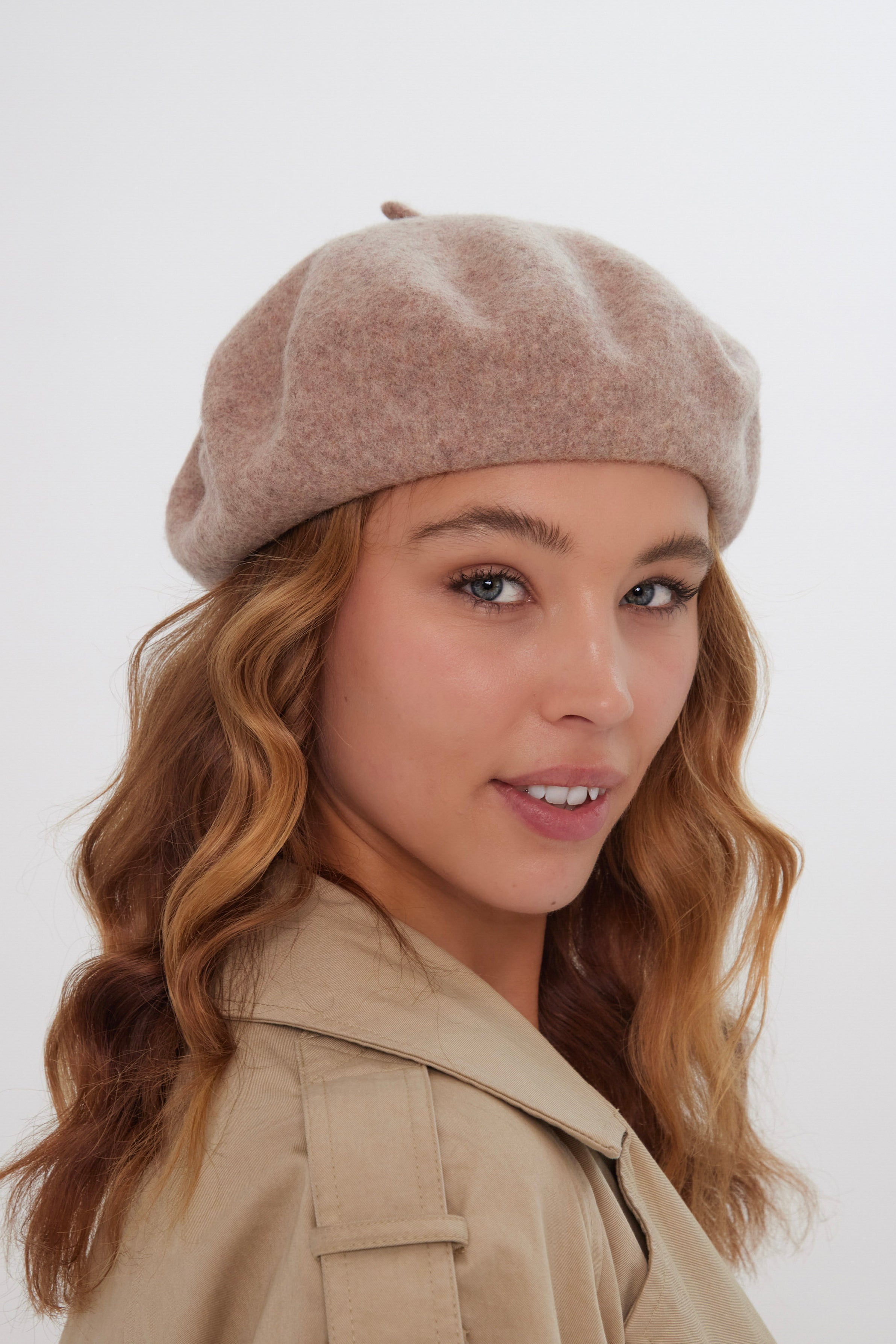 Woman wearing a beige beret and coat against a white background
