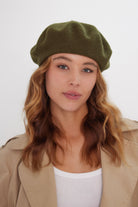 Woman wearing a green beret and beige coat against a white background