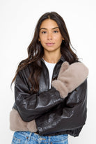 Model wearing fluffy Fur Mittens in Taupe and a brown leather jacket and jeans