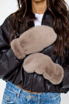 Model wearing fluffy Fur Mittens in Taupe and a brown leather jacket and jeans