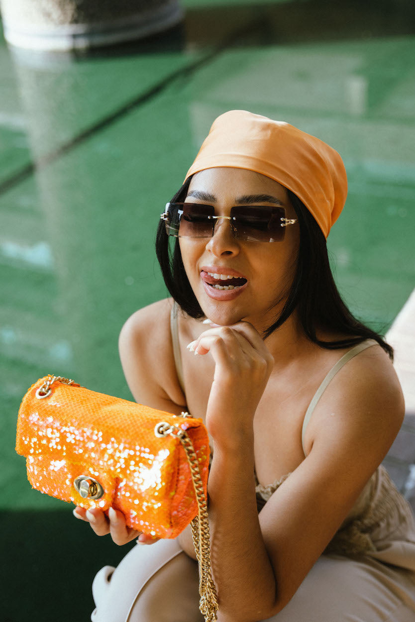 Woman holding an orange handbag with a blurred green background